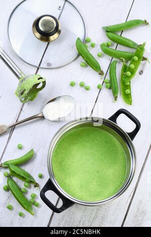 Kochtopf mit frisch gekochter Suppe aus pürierten grünen Erbsen und Sahne auf dem Tisch. Stockfoto