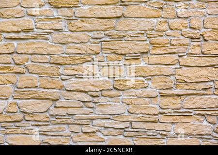 Textur der Steinwand der Fassade des Gebäudes mit Fliesen in Schichten von gelben Naturstein dekoriert. Stockfoto