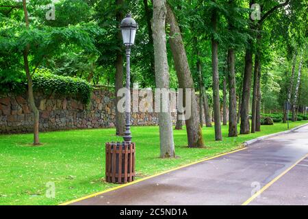 Asphaltstraße mit gelber Markierung einer Fahrspur für das Radfahren auf der Seite einer eisernen Laterne mit einem Holzmüll. Stockfoto