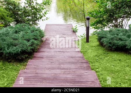 Holztreppen hinunter zum Pier am Fluss, ein Hang mit einer Landschaft von grünen Büschen und einer Wiese mit Laterne, Blick von oben. Stockfoto