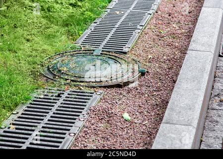 Runde Schachtabdeckung des Drainagesystems auf der Seite der Straße mit einem Eisengitter und Kieselsteinen. Stockfoto