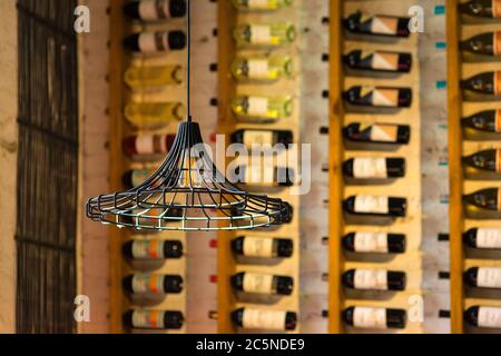 Schwarzer Metall hängenden Loft Kronleuchter im Inneren eines Weinrestaurants im Hintergrund in der Unschärfe Regal mit Flaschen Wein. Stockfoto