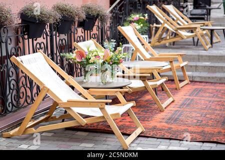 Eine hölzerne Chaiselongue mit Textilien in der Straße ist auf dem Bürgersteig einer Fliese mit Teppich, ein Outdoor-Café mit Sonnenliegen und Holztischen mit einem Stockfoto