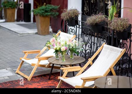 Eine Chaiselongue auf der Straße der Stadt am Gebäude des Hotels ist eine Holzliege mit einem runden Tisch und einer Vase mit Blumen. Stockfoto