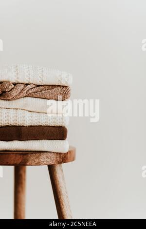 Frauen Mode Komposition. Warme Winter weibliche Wollpullover, Pullover auf einem Holzhocker auf weißem Hintergrund. Modernes Kleidungskonzept Stockfoto