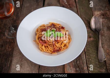 Pasta Carbonara. Spaghetti mit Speck, Parmesankäse und Basilikumblättern. Pasta Carbonara auf weißem Teller mit Parmesan auf dunklem Hintergrund. Italienisches Speisekonzept. Stockfoto