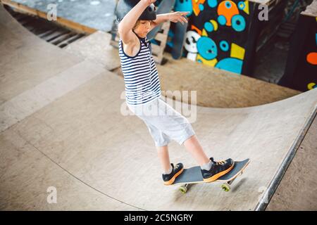 Kinder Skateboarder beim Lernen Tricks auf einer Rampe in einem städtischen Skatepark. Junge in einem Sporthelm reitet auf einem Skateboard an einem Sportplatz. Aktiv Stockfoto