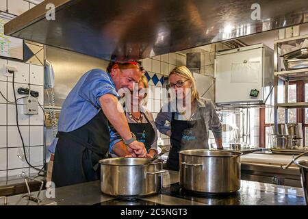 Der mit einem Michelin-Stern ausgezeichnete Koch Thomas Kellermann rührt in einem Topf, während die Kursteilnehmerin Petra (links) und die Journalistin Angela Berg (rechts) in der Küche von Schloss Wernberg in Wernberg-Köblitz, Oberpfalz, Deutschland zuschauen. Stockfoto