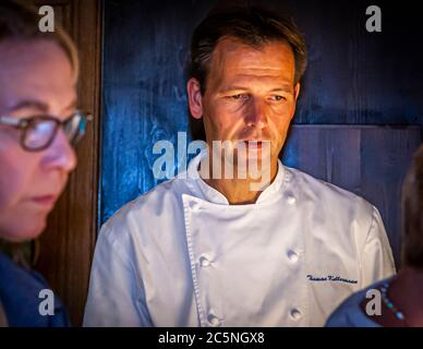 "Und immer dieser Blick.“ Der mit einem Michelin-Stern ausgezeichnete Koch Thomas Kellermann schaut konzentriert zu; ein Teilnehmer des Kochkurses sitzt verschwommen im Vordergrund. Burg Wernberg, Wernberg-Köblitz, Oberpfalz, Deutschland. Seine Kochjacke trägt den gestickten Namen „Thomas Kellermann“. Stockfoto