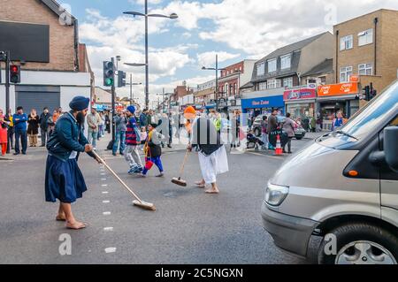 Eifrige Anhänger ziehen ihre Schuhe aus, um die Straße sauber zu fegen, nehmen am Festival von Vaisakhi Teil und feiern die Geburt von Sikhs Stockfoto