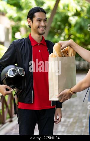 Asiatische Lieferung Mann abholen Bäckerei Lebensmittelbeutel aus Bäckerei Shop zu Kunden, die online bestellen zu liefern. Online-Service-Konzept für die Lebensmittelzustellung in n Stockfoto