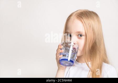 Ein schönes Mädchen von kaukasischen Aussehen trinkt Wasser aus einem Glas auf weißem Hintergrund. Ein junges blondes Model-Mädchen hält ein Glas Wasser. Stockfoto