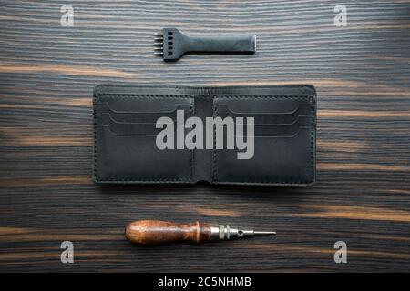 Handgemachte schwarze Ledertasche, Punsch und Ahle auf einem Holztisch. Stockfoto