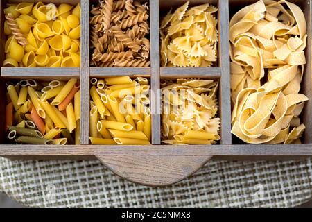 Auswahl der Pasta Draufsicht auf gefüllte Zellen einer Holzkiste mit Zutaten, Nahaufnahme der italienischen Lebensmittel auf dem Tisch stehen. Stockfoto