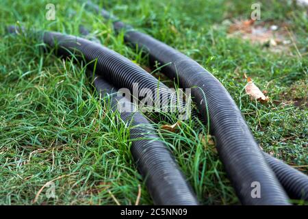 PVC-Wellrohr für Kommunikation, liegt schwarze Rohr auf dem grünen Gras Nahaufnahme. Stockfoto