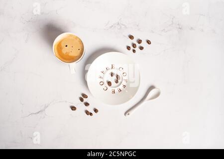 Kaffee / Espresso / Cappuccino Tasse mit Untertasse, Löffel und Kaffeebohnen auf einem weißen Marmortisch Stockfoto