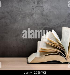 Ein großes, dickes Hardcover-Buch liegt auf einem hellen Holztisch. Das Buch ist offen, die Blätter der Seite sind ausgespannt, und die Rückseite ist ein schwarzer Hintergrund Stockfoto