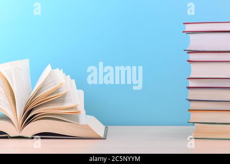 Ein großes, dickes Hardcover-Buch liegt auf einem hellen Holztisch. Das Buch ist offen, neben einem Stapel geschlossener Bücher, und auf der Rückseite ist ein blauer Hintergrund Stockfoto