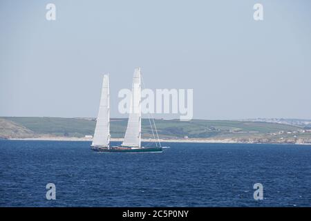 Super Yacht mit 'Soft Wing' Segeln unterwegs in St Ives Bay Blue Sea Headland im Hintergrund Hellblauer Himmel Landschaft Format Stockfoto