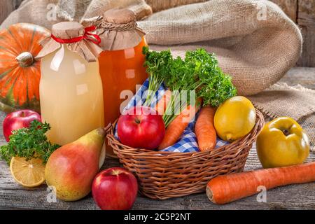 Verschiedene Saftflaschen mit reifen Früchten und Gemüse auf dem rustikalen Tisch und vor dem Leinenhintergrund. Das Konzept der gesunden Ernährung. Stockfoto