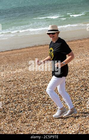 Southsea, Portsmouth, England, Großbritannien. 2020. Ältere Frau am Strand laufen tragen, halten Sie Ihre Distanz T-Shirt während der Covid-19 Epidemie. Stockfoto