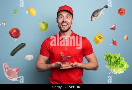 Deliveryman hält einen kleinen Wagen, der mit Nahrung gefüllt ist. Cyan-Hintergrund. Stockfoto