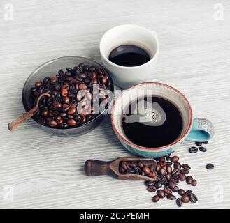 Kaffeetassen und Kaffeebohnen auf hellem Holz Küchentisch Hintergrund. Stillleben mit Kaffee. Stockfoto