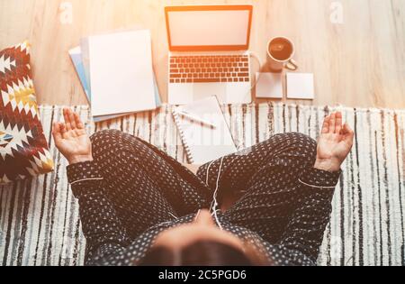 Geschäftsfrau in Pyjamas gekleidet meditieren mit Morgenkaffee mit Gyan Mudra Palmen.auf dem Boden Büro mit Laptop, Papiere Draufsicht erschossen. Entfernung Stockfoto