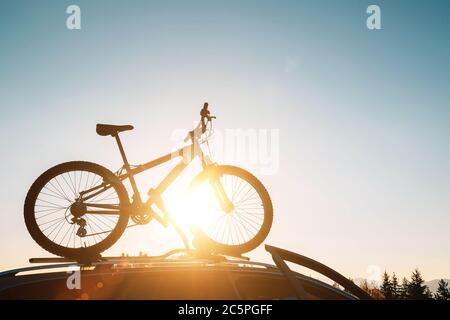 Montierte Mountainbike Silhouette auf dem Autodach mit Abend Sonne Licht Strahlen Hintergrund. Sichere Sportartikel Transport mit einem Auto Konzept Bild. Stockfoto