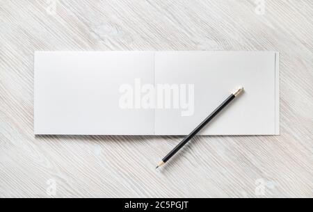 Foto eines offenen Skizzenbuches mit leeren Seiten und Bleistift auf hellem Holzhintergrund. Draufsicht. Flach liegend. Stockfoto