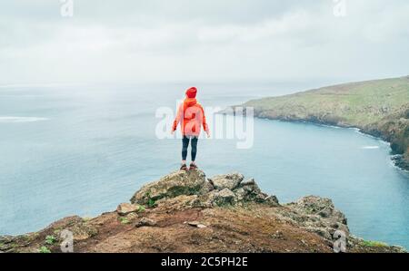 Trail Runner Damen gekleidet orange sportliche Hoodie und rote Mütze auf der Klippe ruhen und genießen Sie den Blick auf den Atlantik auf Ponta de Sao Lourenço Halbinsel Stockfoto