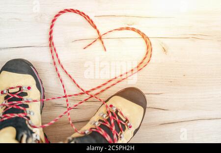 Konzeptionelles Bild des Paares neue Trekkingstiefel auf dem Holzboden Hintergrund mit freigelassenen langen Schnürsenkeln hinter in Herzform liegend. Stockfoto