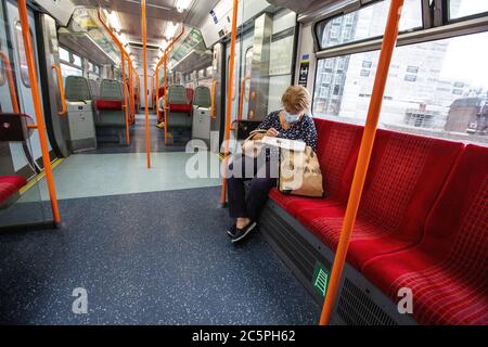 Eine Dame sitzt beim Lesen ihrer Zeitung, während sie eine obligatorische Gesichtsmaske trägt, während sie mit einem leeren Wagen auf den South West Zügen öffentlichen Verkehrsmitteln UK reist Stockfoto