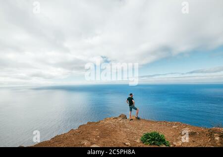 Aktiver Reisender Mann gekleidet schwarzes T-Shirt genießen Atlantik Blick auf der westlichen Halbinsel Punkt der Insel Madeira - Ponta do Pargo, Portugal. Stockfoto