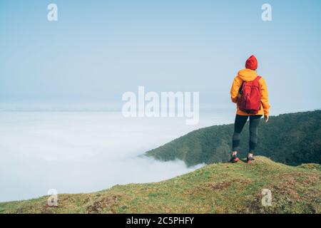 Junge Backpacker-Frau gekleidet orange wasserdichte Jacke Wandern am Berg über der Wolke Route Ende Februar auf Madeira Insel Portug Stockfoto