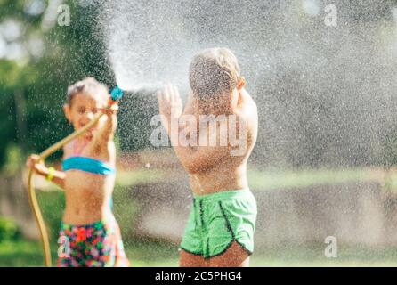 Junge und Mädchen spielen im Garten, Gießen mit Wasser einander aus dem Schlauch, so dass ein Regen. Happy Kindheitskonzept Bild. Stockfoto