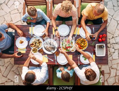 Großes Familienessen mit mehreren Generationen im Prozess. Bild von oben auf dem Tisch mit Essen und Händen. Lebensmittelkonsum und generationsübergreifendes Familienkonzept ima Stockfoto