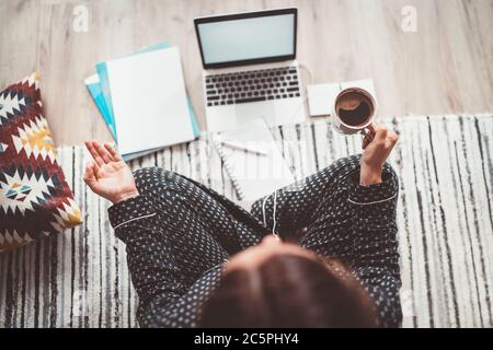 Geschäftsfrau in Pyjamas gekleidet meditieren mit Morgenkaffee mit Gyan Mudra Palmen.auf dem Boden Büro mit Laptop, Papiere Draufsicht erschossen. Entfernung Stockfoto