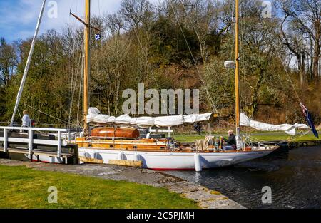 Segelyacht mit Paar an Bord, die durch die Schleuse auf dem Crinan Canal, Argyll, Schottland, Großbritannien Stockfoto