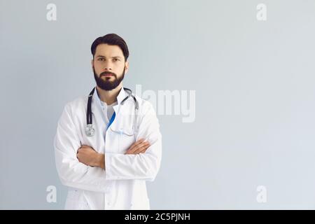 Seriöser Arzt mit gekreuzten Armen auf grauem Hintergrund, kopieren Sie Leerzeichen Text. Junger Arzt, Kinderarzt oder Krankenschwester Stockfoto