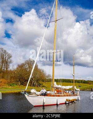 Segelyacht mit Paar an Bord, die durch die Schleuse auf dem Crinan Canal, Argyll, Schottland, Großbritannien Stockfoto