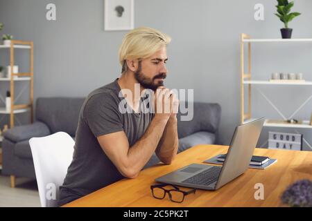 Junger Mann, der im Heimbüro am Laptop arbeitet. Millennial Mann bei der Durchführung von Online-Konferenzen oder Geschäftstreffen Stockfoto
