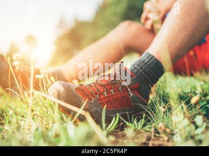 Trekkingschuhe für Rucksacktouristen aus nächster Nähe. Mann hat eine Pause auf grünem Gras sitzen und genießen Bergwandern, aktiv Sport Rucksackwandern Gesundheit Stockfoto