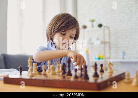 Smart Boy spielt Schach am Tisch im Zimmer. Das Kind spielt Brettspiele. Stockfoto