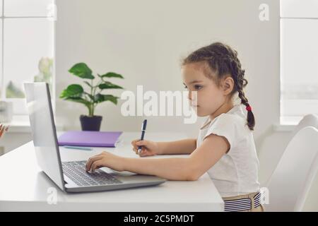 Online-Lernen. Entfernte Schule für Kinder. Ein kleines Mädchen benutzt einen Laptop-Videounterricht, während es an einem Tisch im Zimmer sitzt. Stockfoto