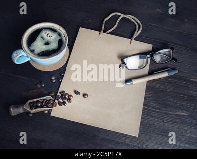 Stillleben mit Kaffeetasse, Kaffeebohnen, Gläsern, Stift und Kraftpapier-Tasche auf Vintage-Holz Hintergrund. Stockfoto