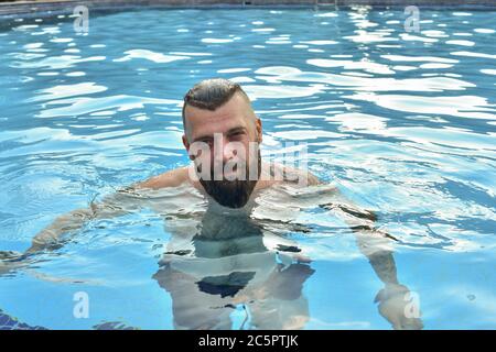 Bärtiger Mann, der in einem Pool schwimmt. Mann mit Bart im Pool. Brunette Mann im Urlaub. Sommerurlaub Konzept Stockfoto
