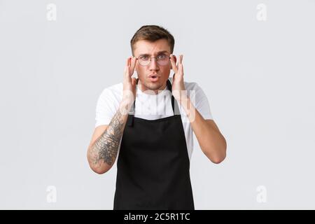 Kleineinzelhandelsinhaber, Café und Restaurant Mitarbeiter Konzept. Fasziniert und unsicher, gutaussehender Kellner, Barista, der sich genauer anschaut, zieht eine Brille an Stockfoto