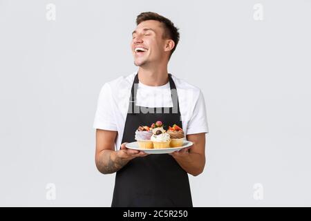 Kleineinzelhandel, Cafés und Bäckereikonzept. Leidenschaftlicher, gutaussehender Barista, Verkäufer im Konditorladen, enge Augen und lächelnd Stockfoto