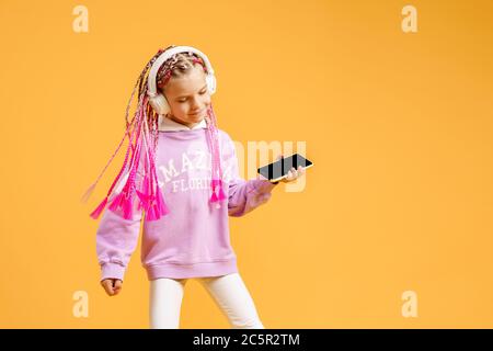 Ziemlich modernes Mädchen mit rosa Dreadlocks in Kopfhörer lächeln und Selfie auf Smartphone isoliert über gelb. Stockfoto